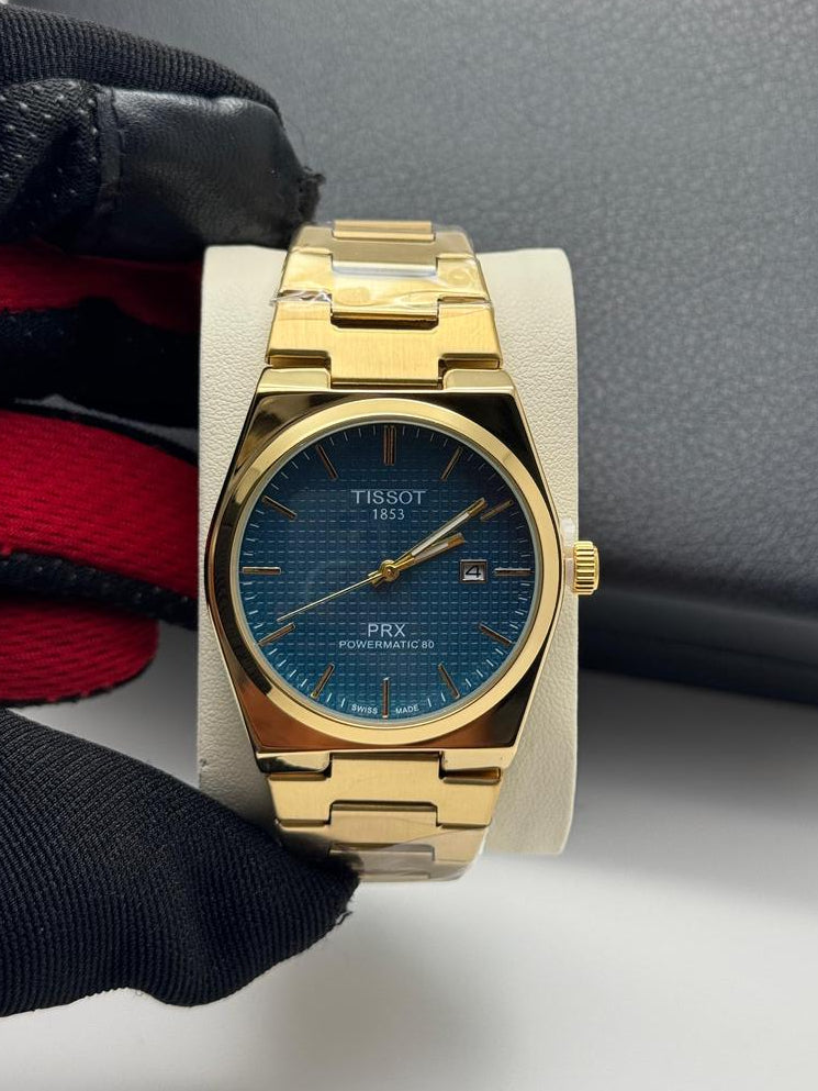 Gold wristwatch with blue face on a white surface with black gloves and gray box in the background