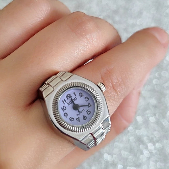 Silver ring with a clock face on a hand against a textured gray background